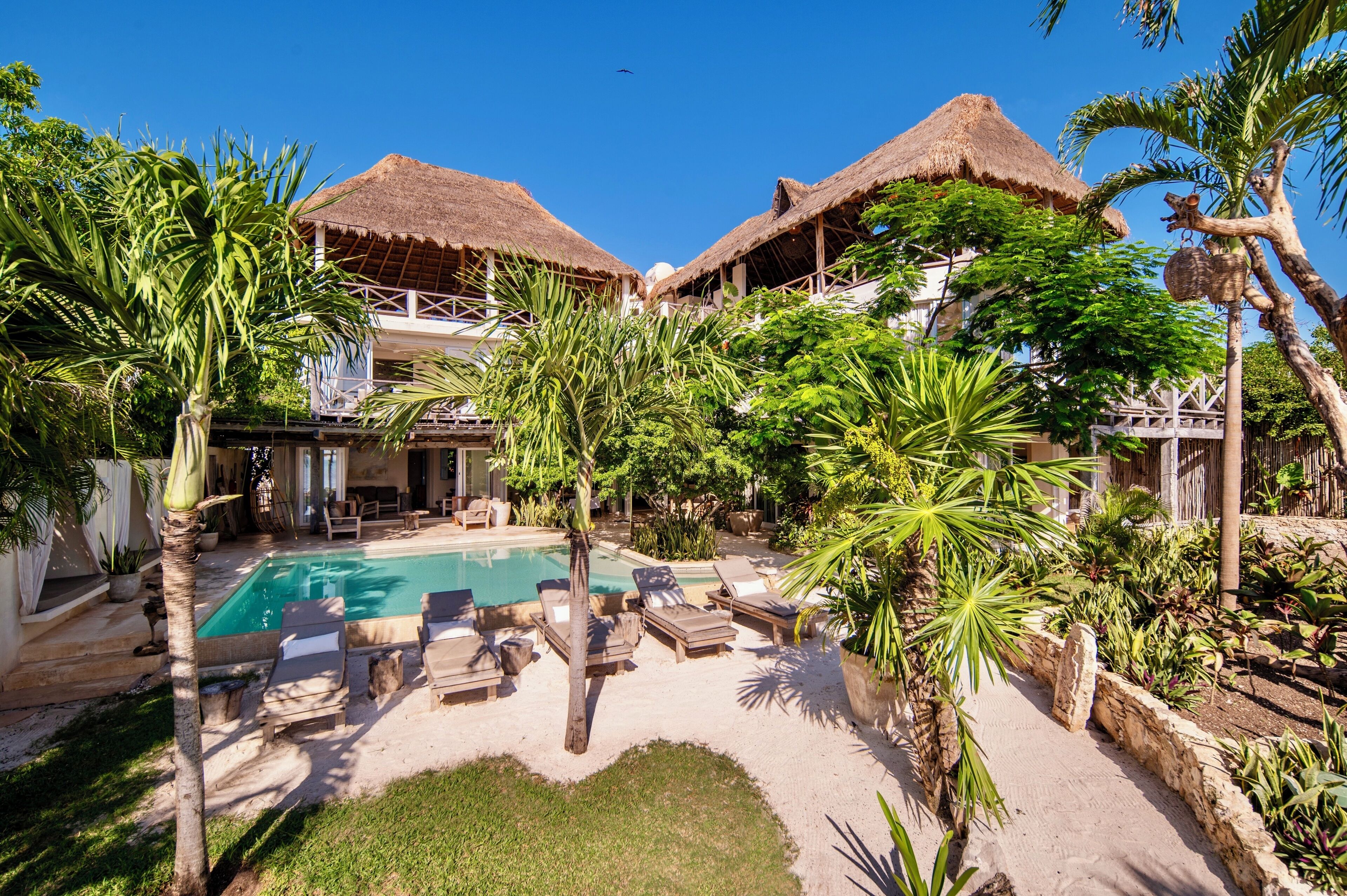 A pool area with lounge chairs and thatched-roof structures.