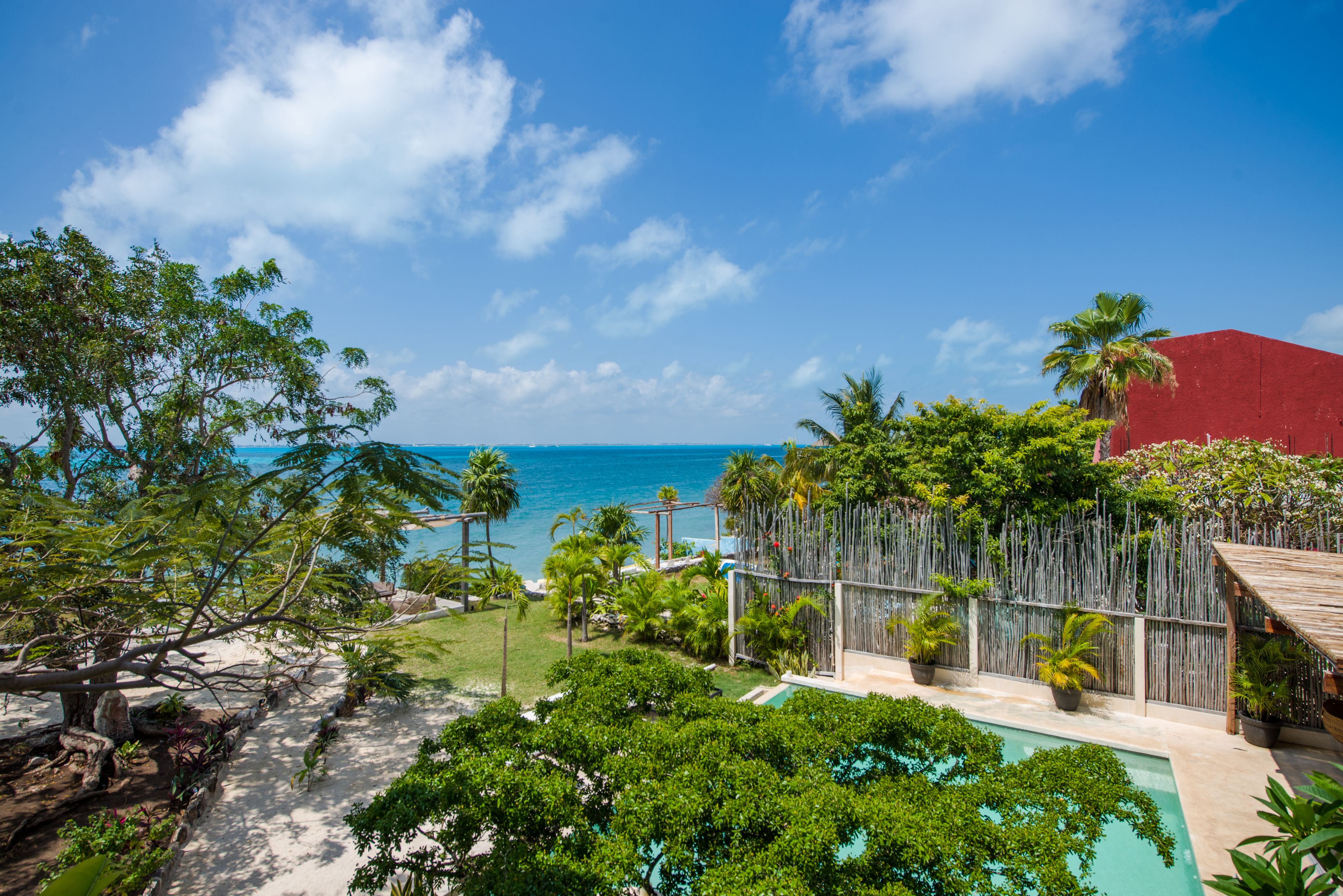 A pool area with a view of the ocean, surrounded by tropical vegetation and a wooden fence.
