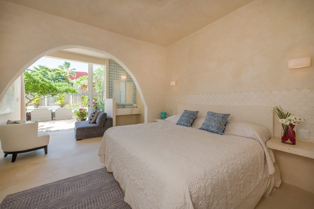 A bedroom with a large bed, a sofa, and a chair. There is a window with a view of the outside.