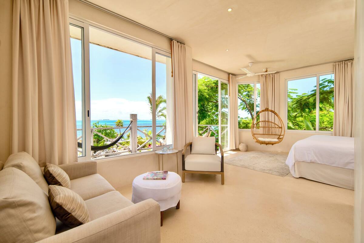 A hotel room with a large window, a bed, a sofa, a chair, and a small table.