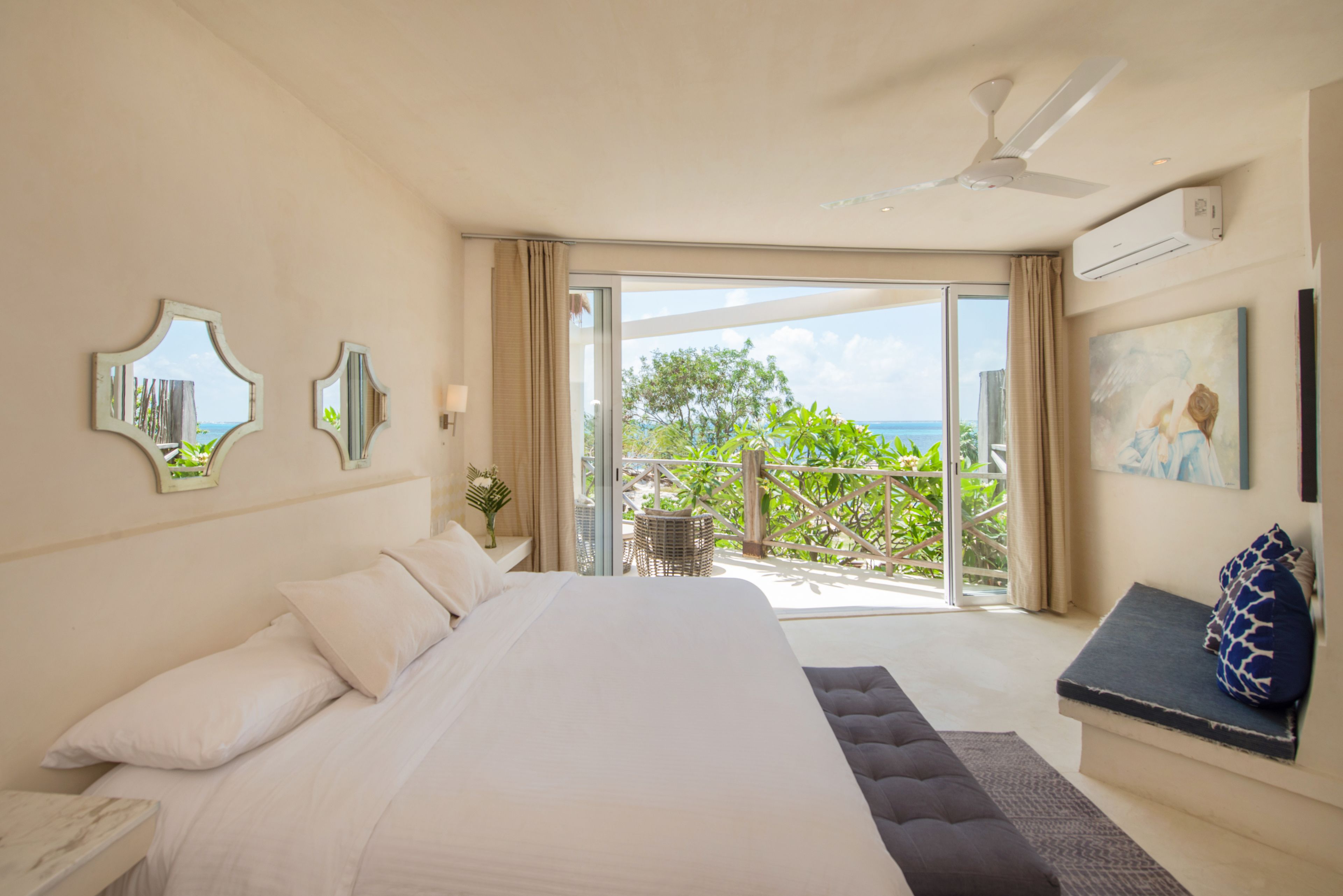 A bedroom with a large bed, a ceiling fan, and a balcony with a view of the sea.