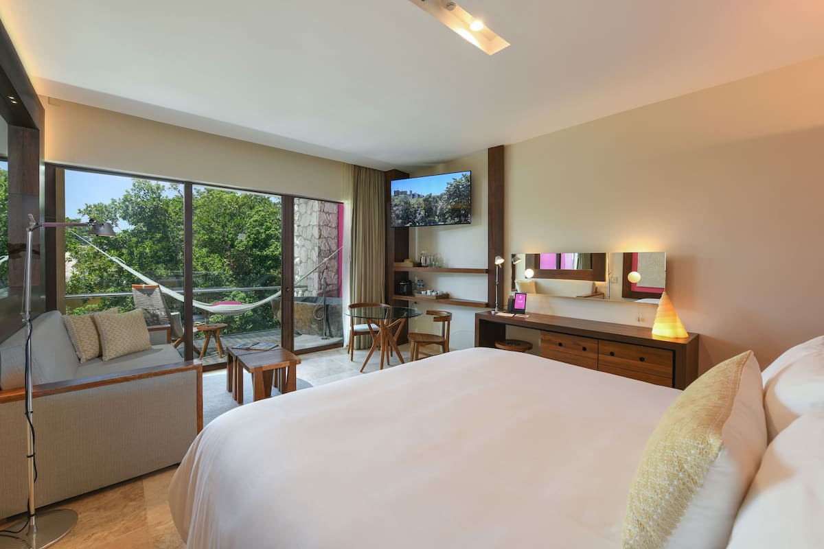 A modern hotel room with a large bed, a balcony with a hammock, a desk, and a TV.