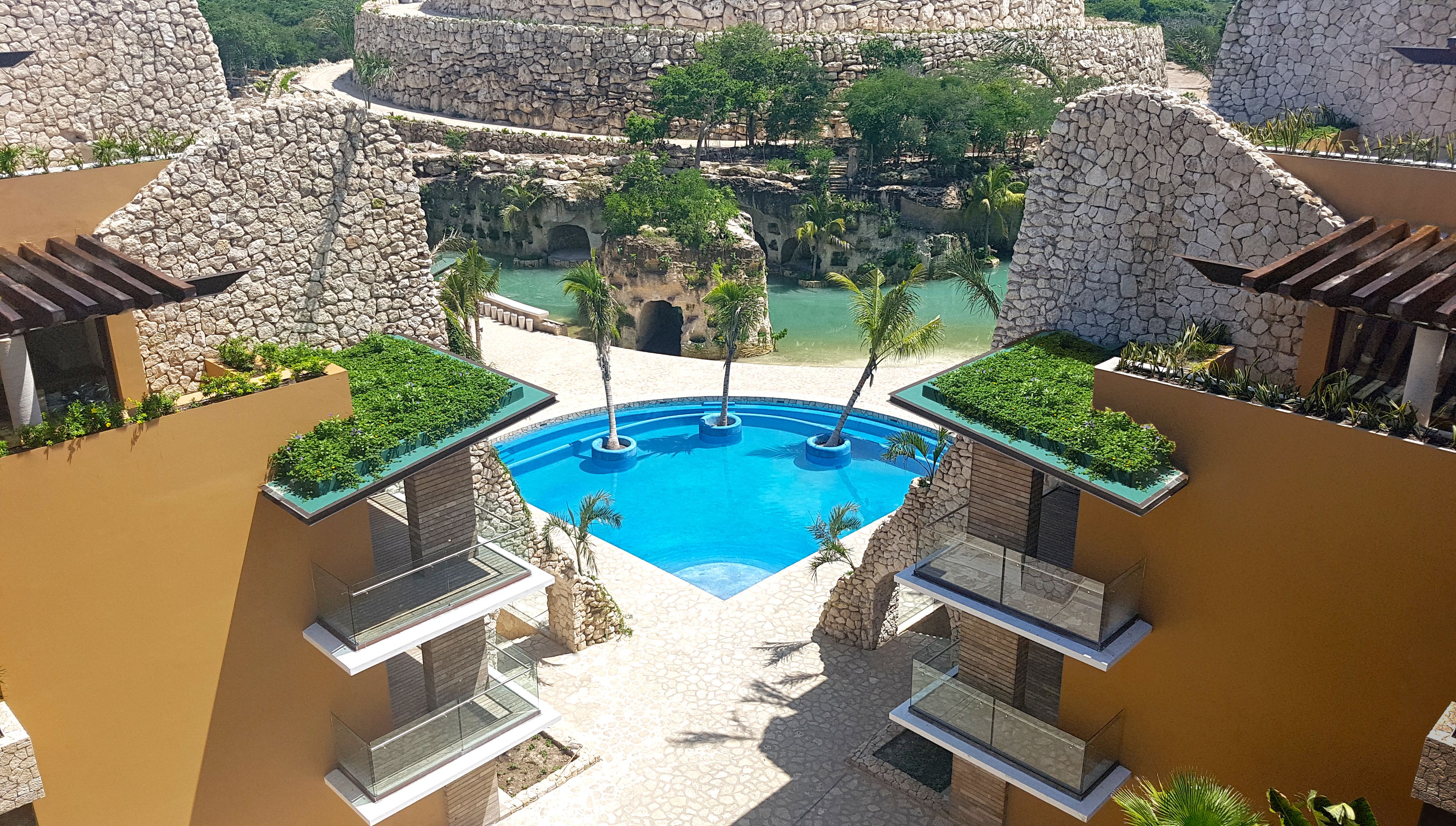 Una piscina en la azotea con aguas cristalinas, rodeada de muros de piedra y palmeras.