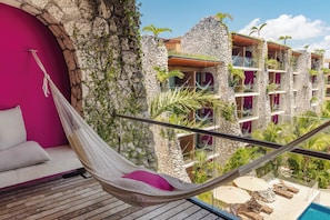 A hammock on a balcony with a view of a pool and a building with stone walls and balconies.