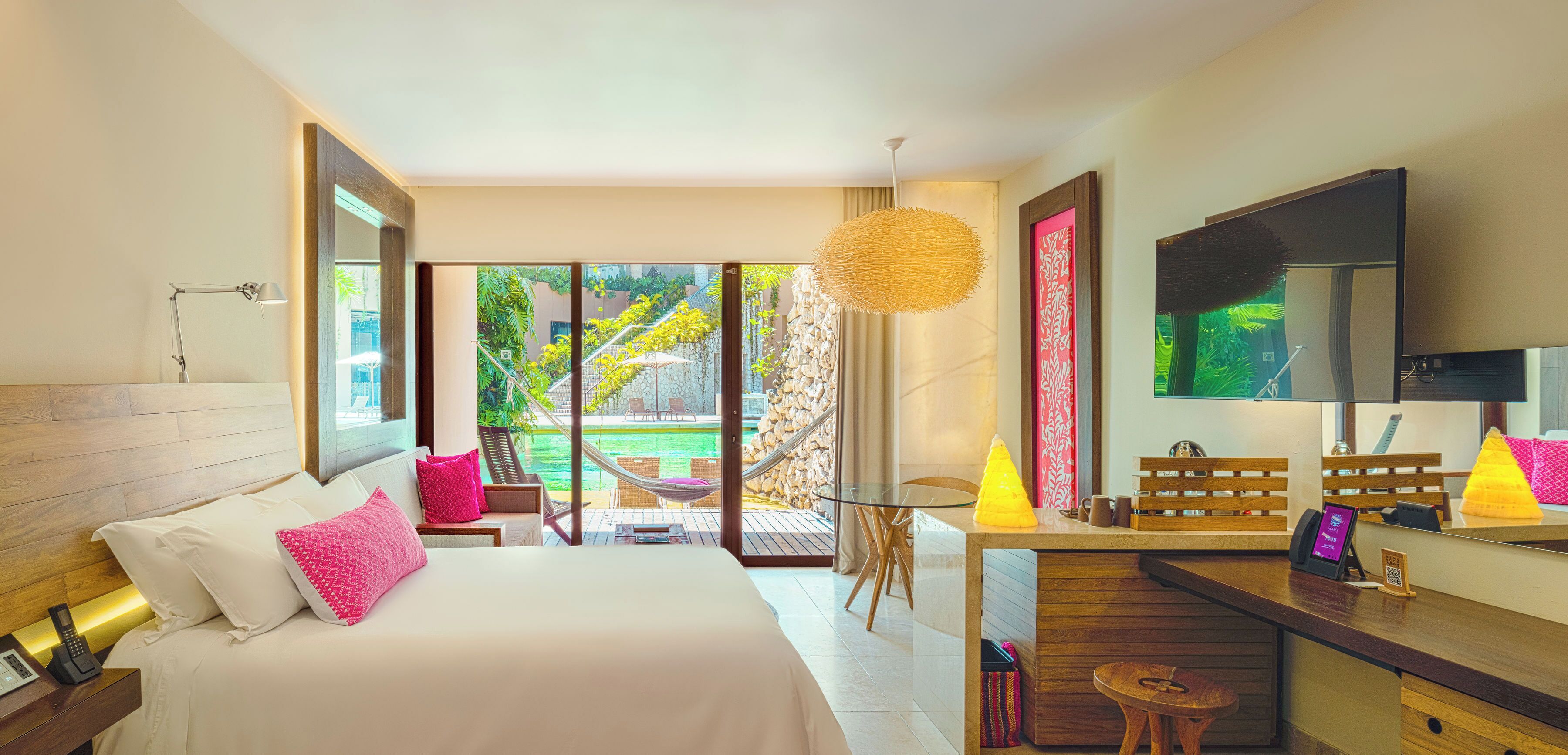 Ein modernes Hotelzimmer mit einem großen Bett, einem Schreibtisch mit Stuhl, einem Fernseher und Blick auf Garten und Pool.