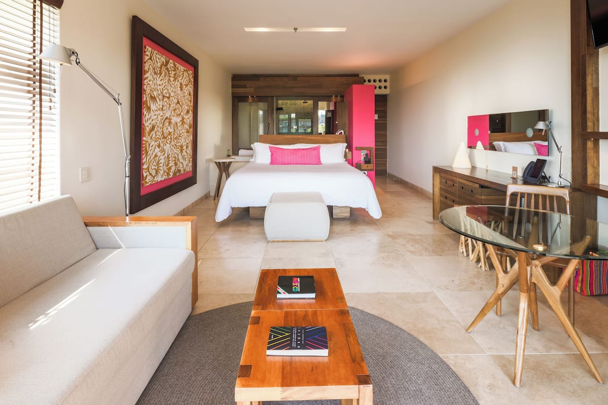 A modern hotel room with a large bed, a sofa, a dining table, and a desk.