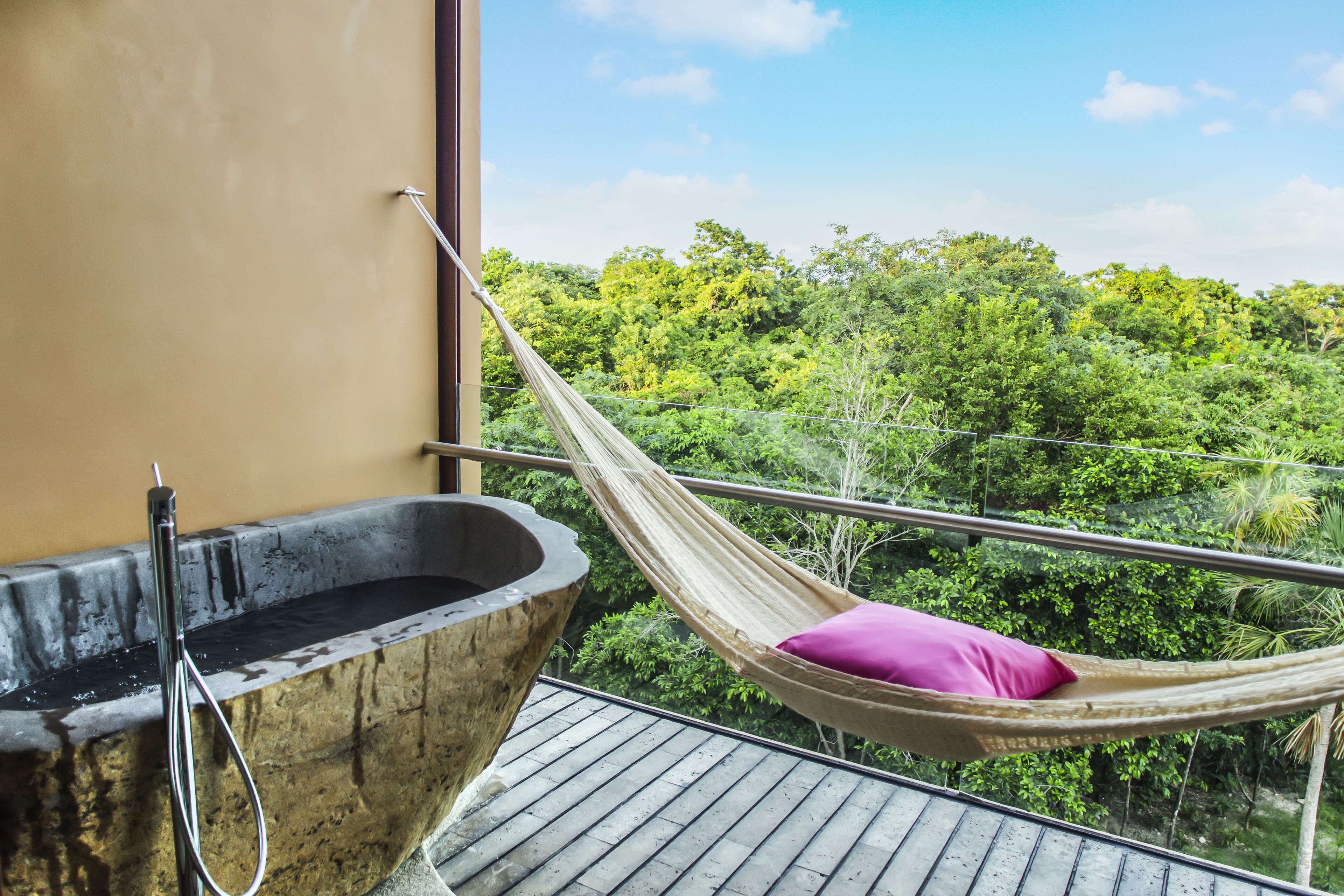 Una hamaca con una almohada rosa en un balcón con vistas a un bosque verde exuberante.