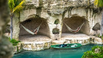 Two hammocks attached to a stone wall with a green kayak in a clear blue pool below.