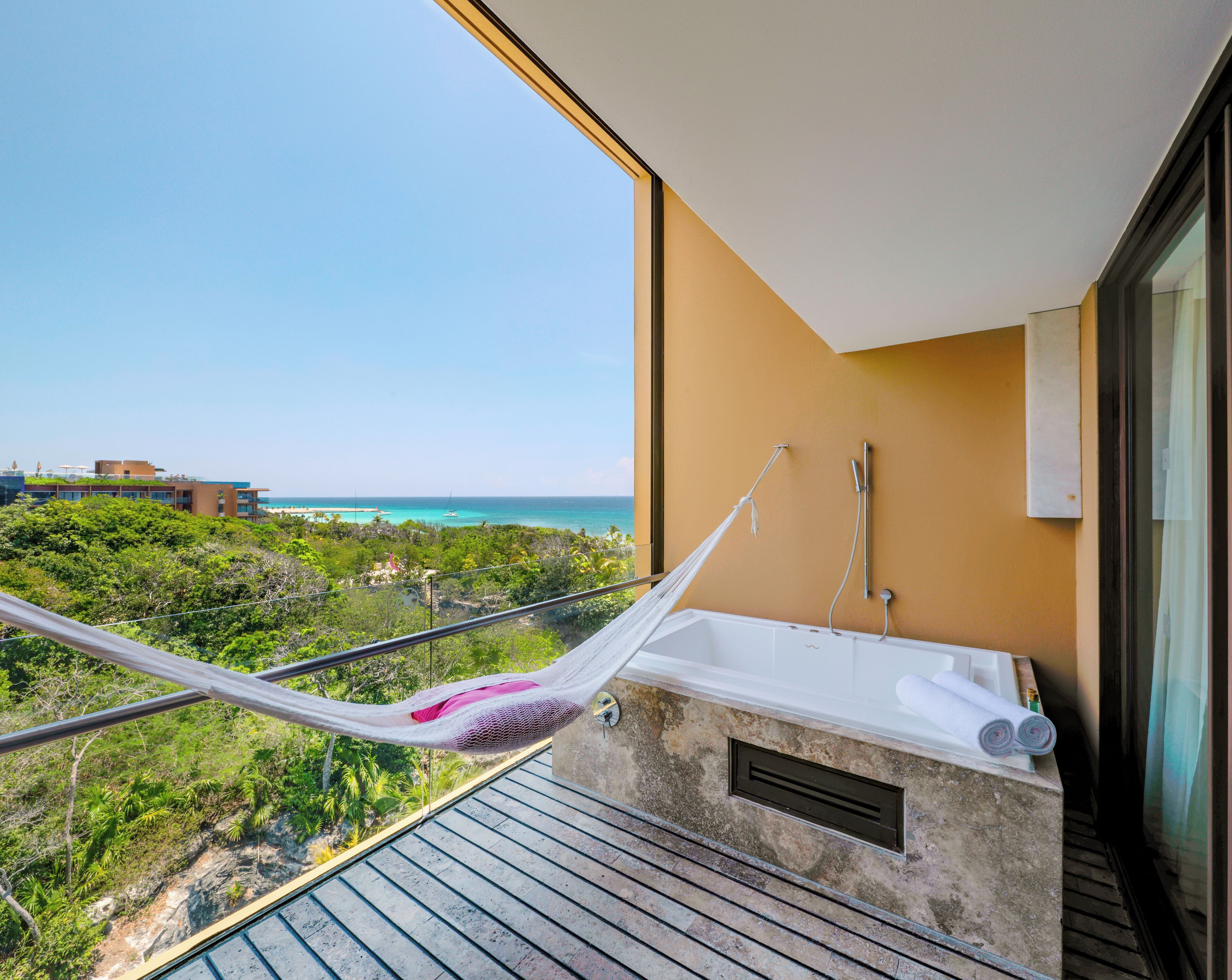 A balcony with a hammock, a bathtub, and a view of the ocean.