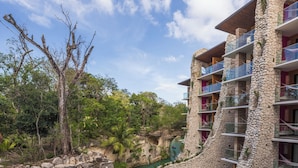A resort with a natural rock bridge over a turquoise pool, surrounded by lush greenery and a clear sky. - Hotel Xcaret Mexico - All Parks / All Fun Inclusive - All inclusive (Playa del Carmen)