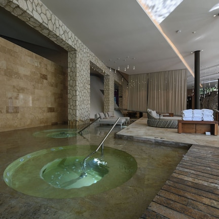 A spa area with a stone wall, a wooden deck, and a seating area with towels.