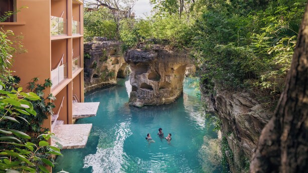A swimming pool surrounded by natural rock formations and lush greenery. - Hotel Xcaret Mexico - All Parks / All Fun Inclusive - All inclusive (Playa del Carmen)
