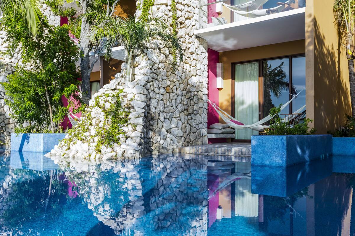 A pool area with a stone wall, a hammock, and a reflection in the water.