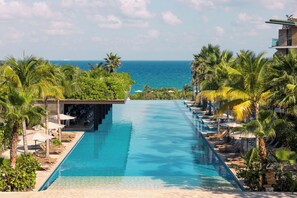 A long swimming pool with a view of the ocean, surrounded by palm trees and lounge chairs. - Hotel Xcaret Mexico - All Parks / All Fun Inclusive - All inclusive (Playa del Carmen)