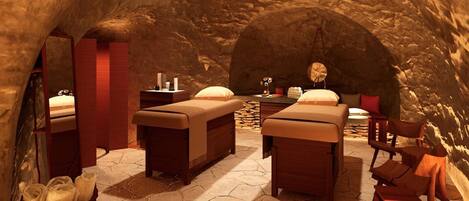 A spa room with two massage tables, a stone floor, and a small table with candles and a mirror.