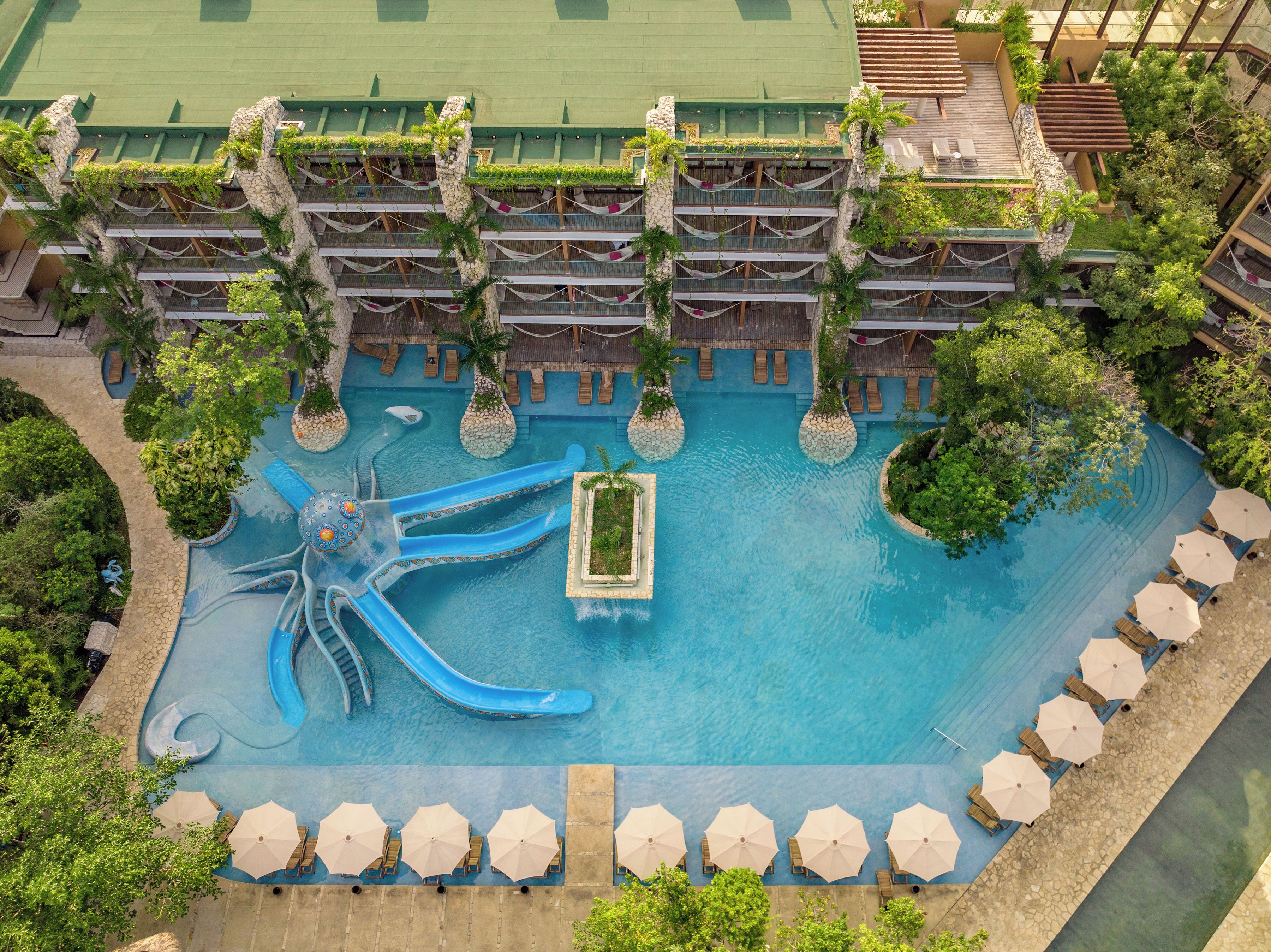 An aerial view of a resort with a central pool, multiple balconies, and surrounding greenery.