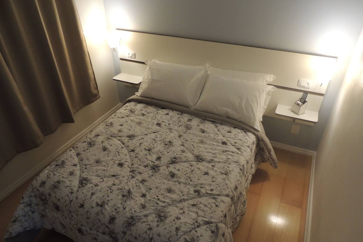 Une chambre à coucher avec une couvre-lit à motifs floraux, deux tables de chevet avec des lampes et un plancher en bois.