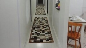 Un pasillo estrecho con alfombra a cuadros, paredes blancas y una silla de madera cerca de una mesa.