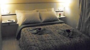 Una habitación de hotel con cama, mesitas de noche, un equipo de aire acondicionado y una cortina.