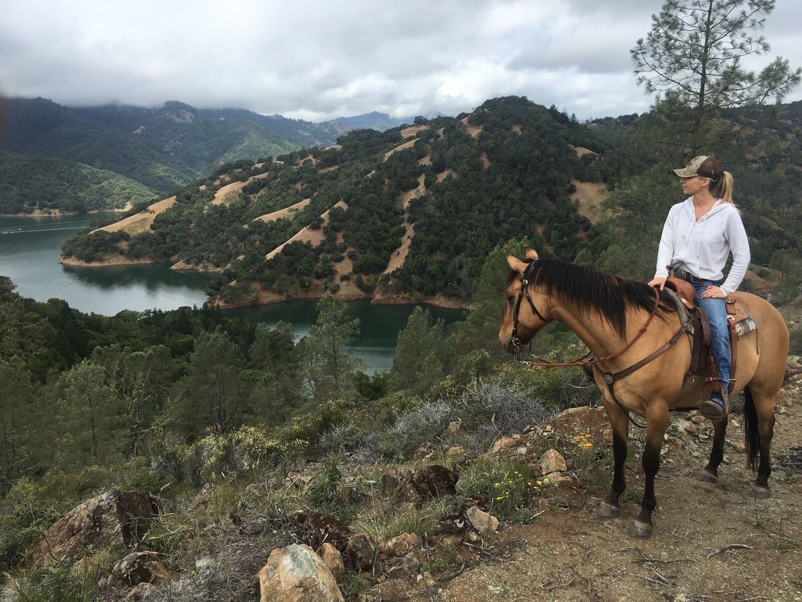 Une personne à cheval sur un chemin de terre, avec un lac et des collines en arrière-plan.