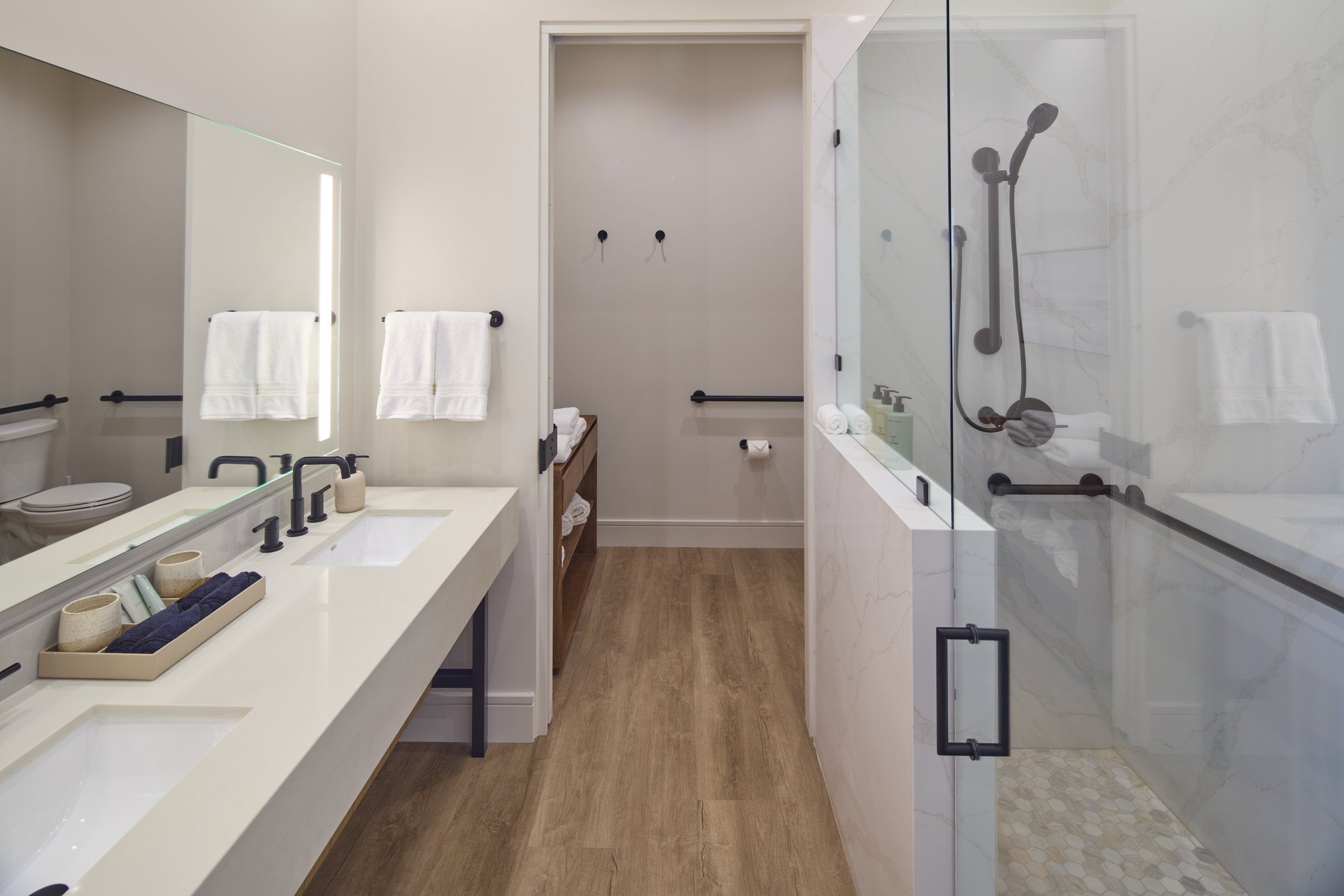 Une salle de bain moderne dotée d’une douche à parois de verre, d’un grand miroir et d’un meuble-lavabo avec un évier et un porte-serviettes.