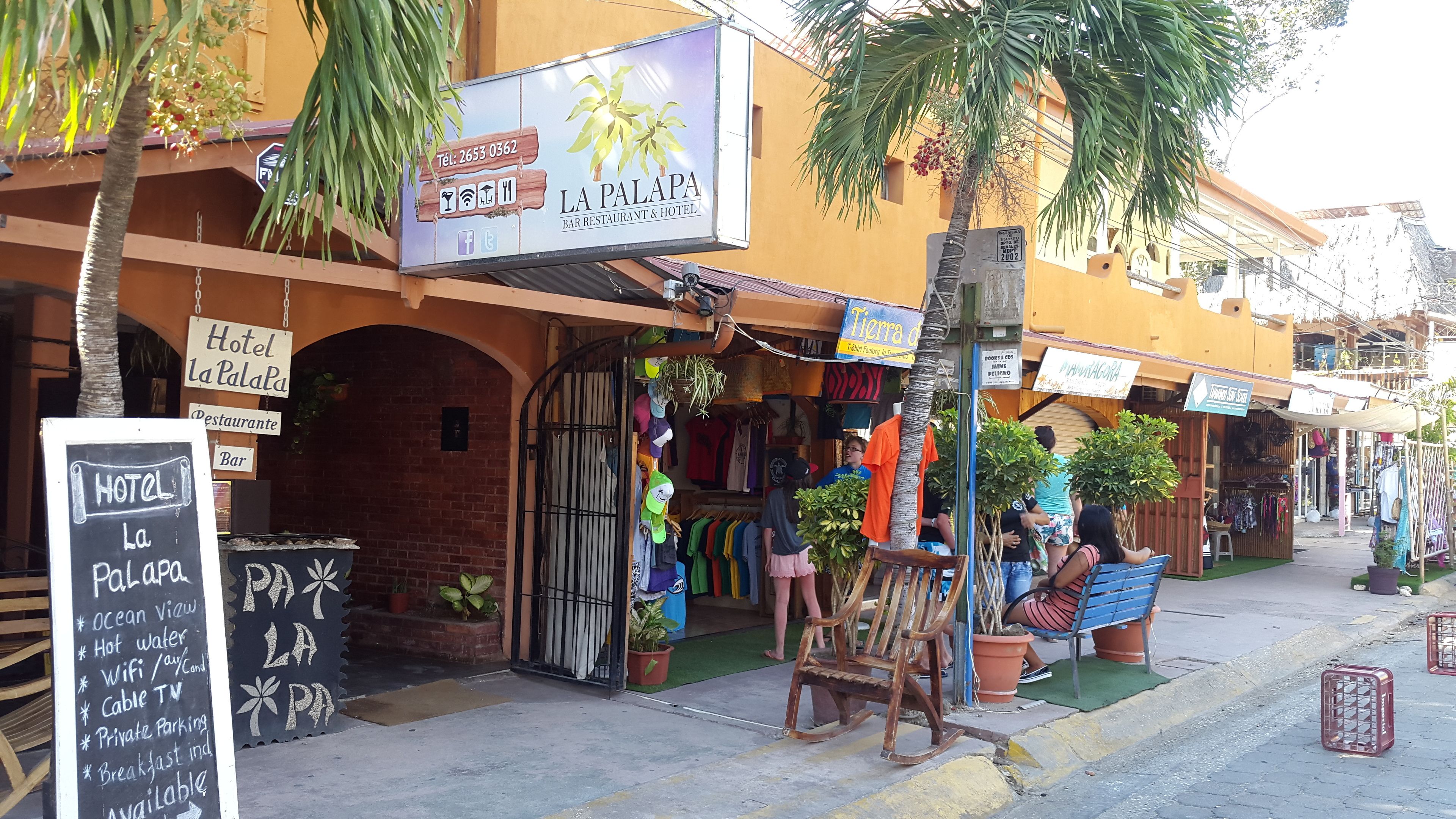 A storefront with a sign for 'Hotel La Palapa' and a variety of clothing items displayed outside.
