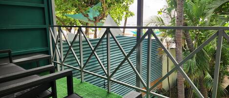 A balcony with a metal railing, green artificial grass, and a view of a building with a corrugated metal roof.