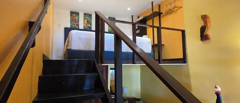 A staircase with a wooden handrail leading to a bed with white bedding.