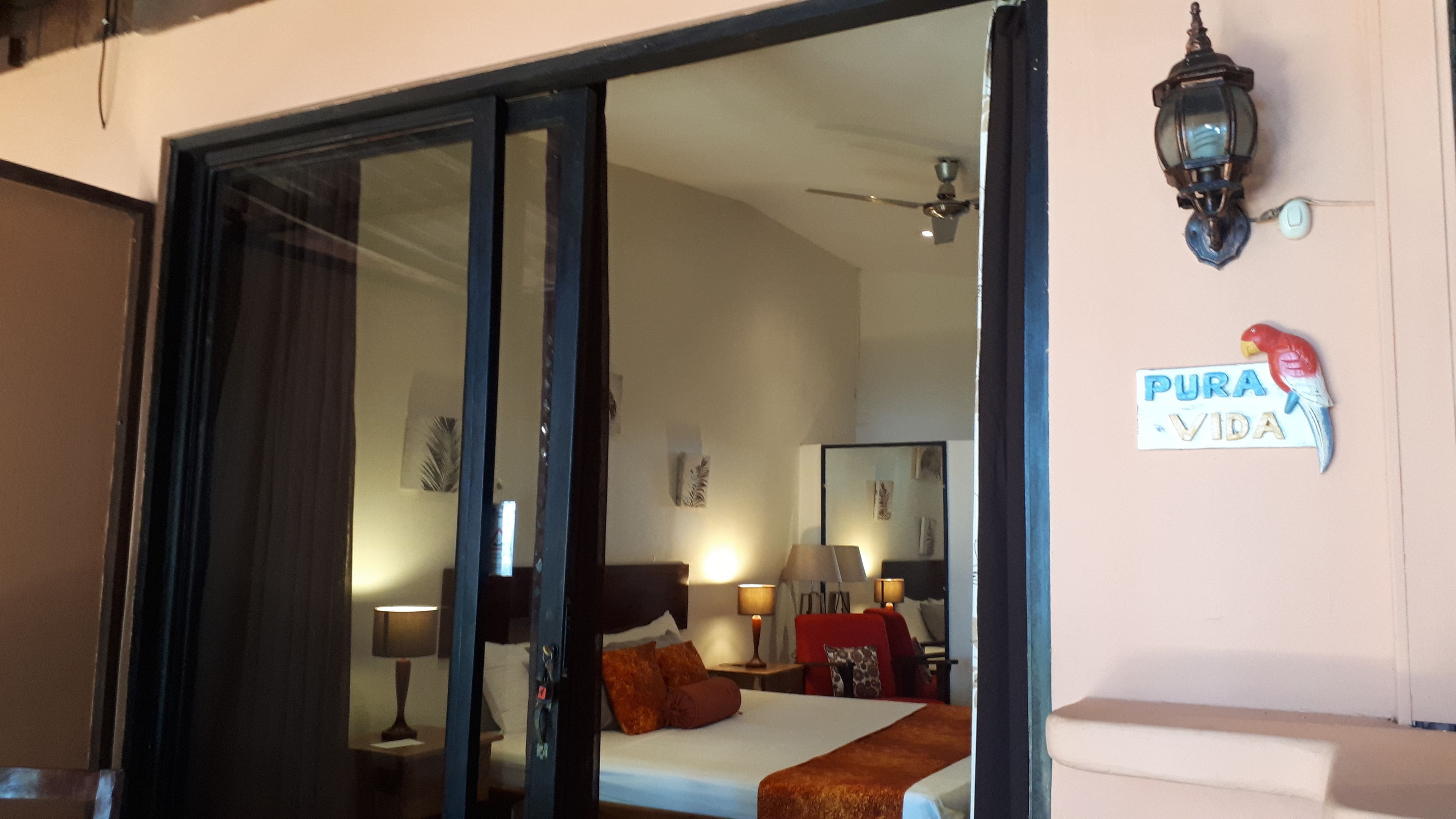 A hotel room with a bed, a nightstand, a lamp, a ceiling fan, and a wall sign.