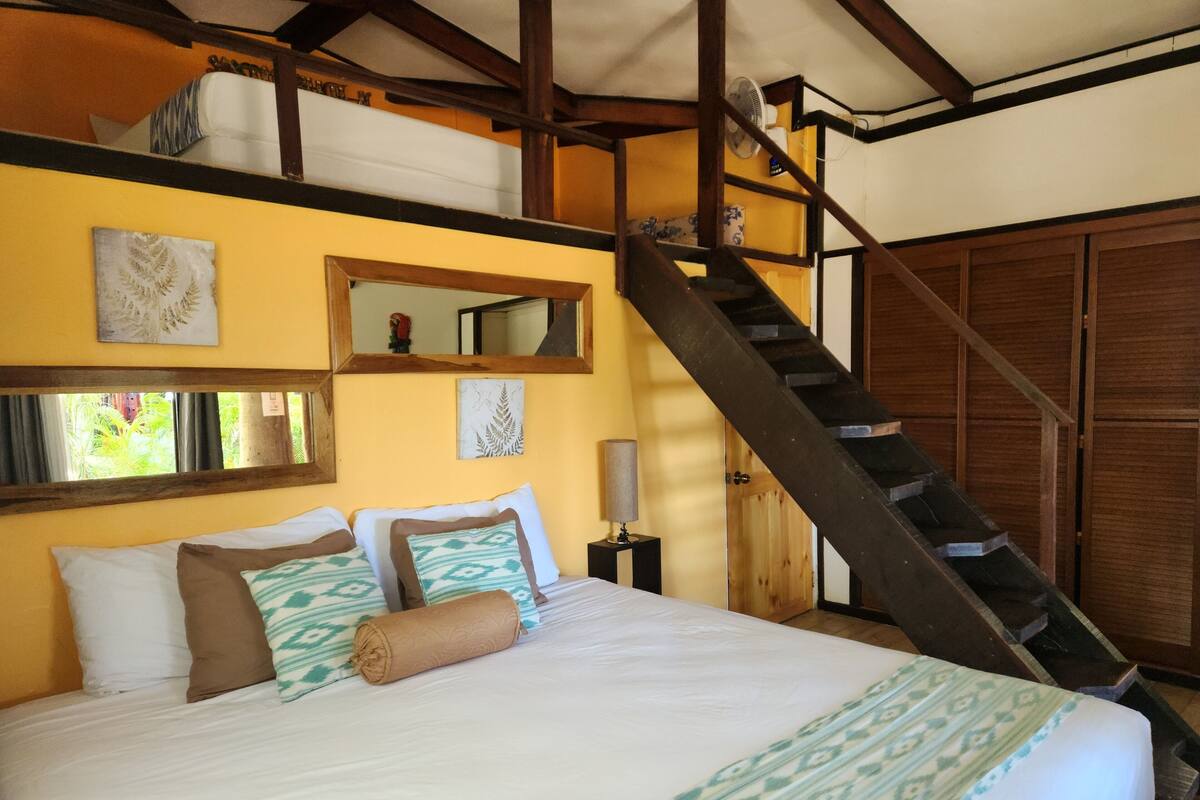 A bed with white and patterned bedding, a wooden headboard, and a staircase leading to an upper level.
