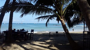 A beachside restaurant with tables and chairs, overlooking the ocean with boats in the distance. - Hotel La Palapa (Tamarindo)