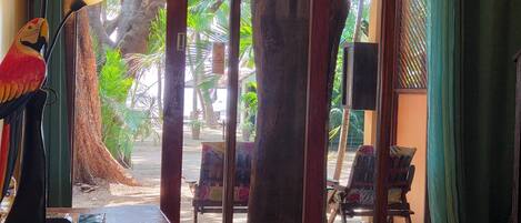 A room with a wooden desk, a lamp, and a view of a tropical garden through a glass door.