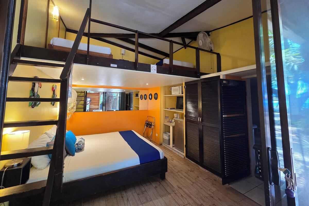 A compact hotel room with a bunk bed, a small desk, a mirror, and a wardrobe.