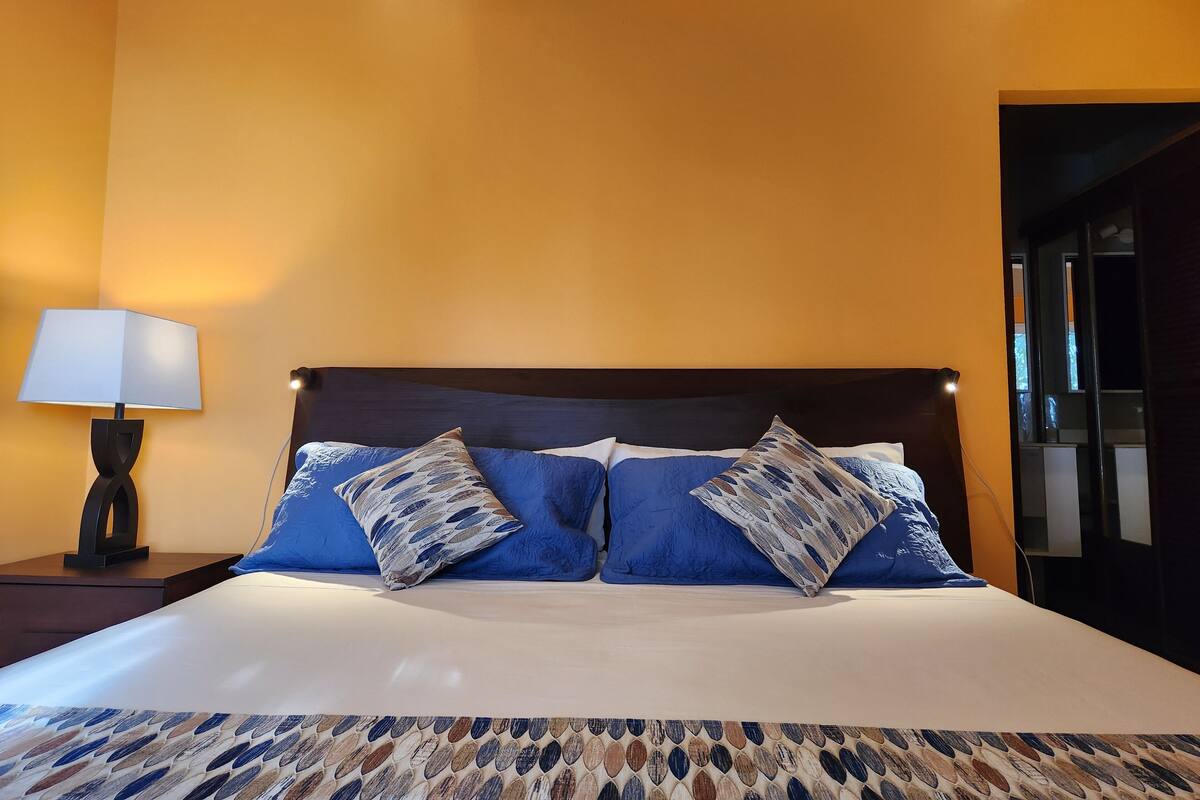 A bed with a patterned bedspread, two pillows, a bedside lamp, and a wooden headboard.