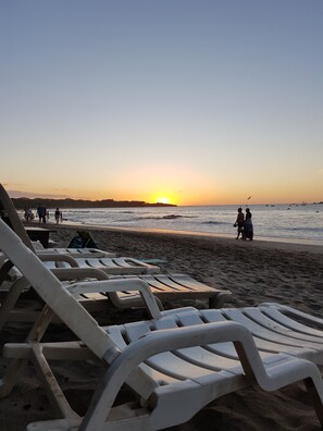 Una playa con tumbonas y un atardecer.