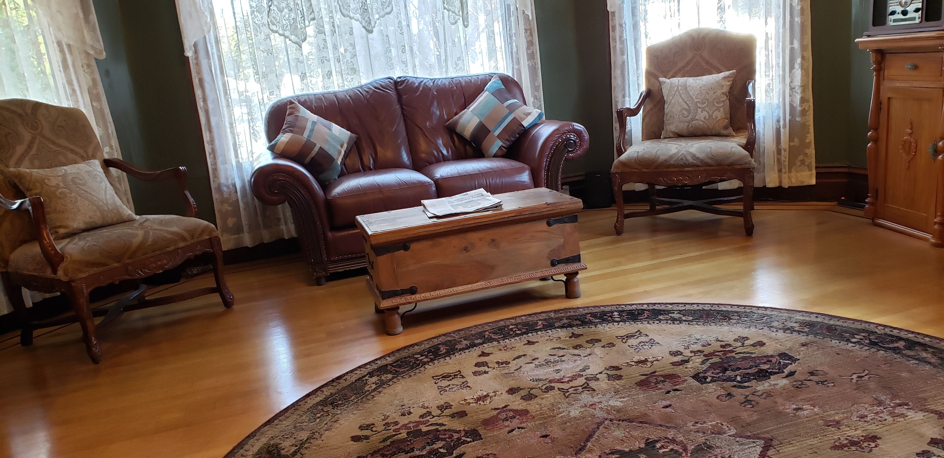 A living room with a brown leather sofa, two armchairs, a wooden coffee table, and a patterned rug.