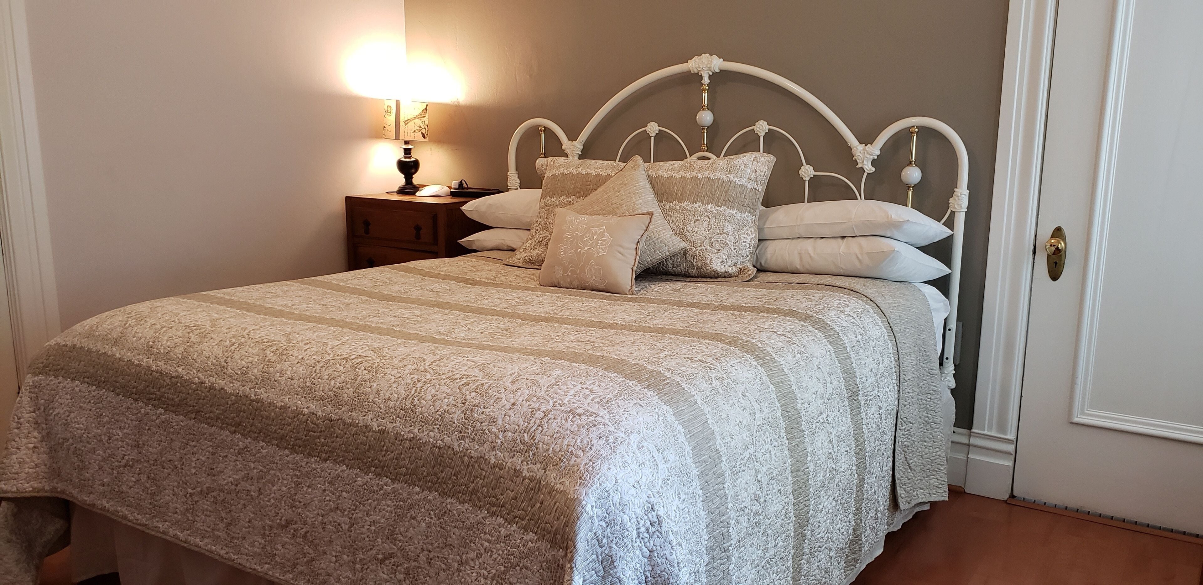 A neatly made bed with a patterned bedspread and multiple pillows, a bedside table with a lamp, and a door with a brass doorknob.