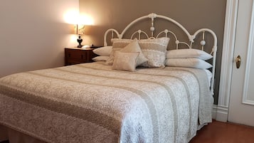 A neatly made bed with a patterned bedspread and multiple pillows, a bedside table with a lamp, and a door with a brass doorknob.