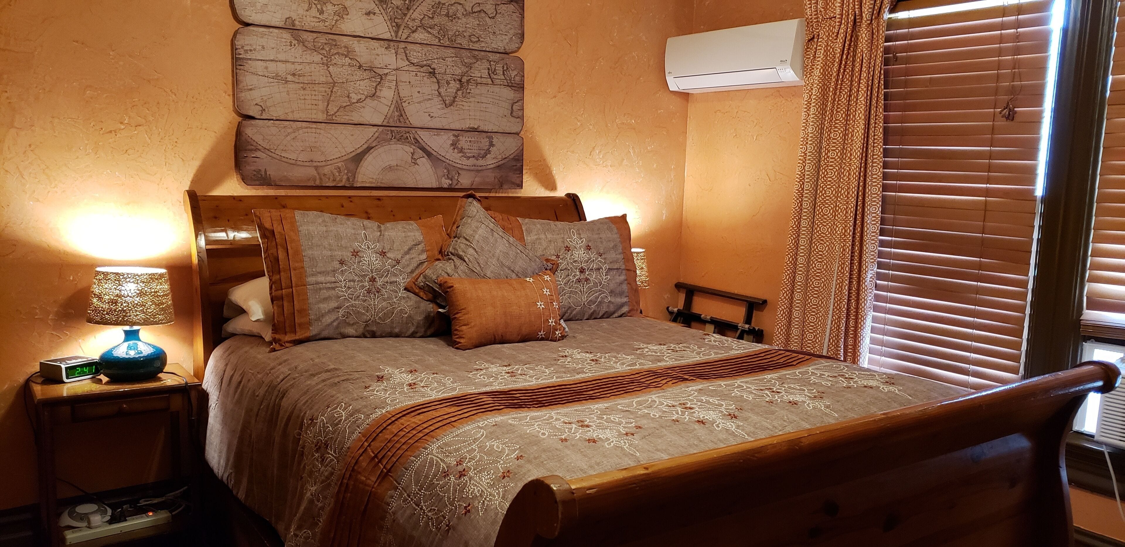 A bedroom with a wooden bed, patterned bedding, a world map artwork, an air conditioner, and a bedside lamp.