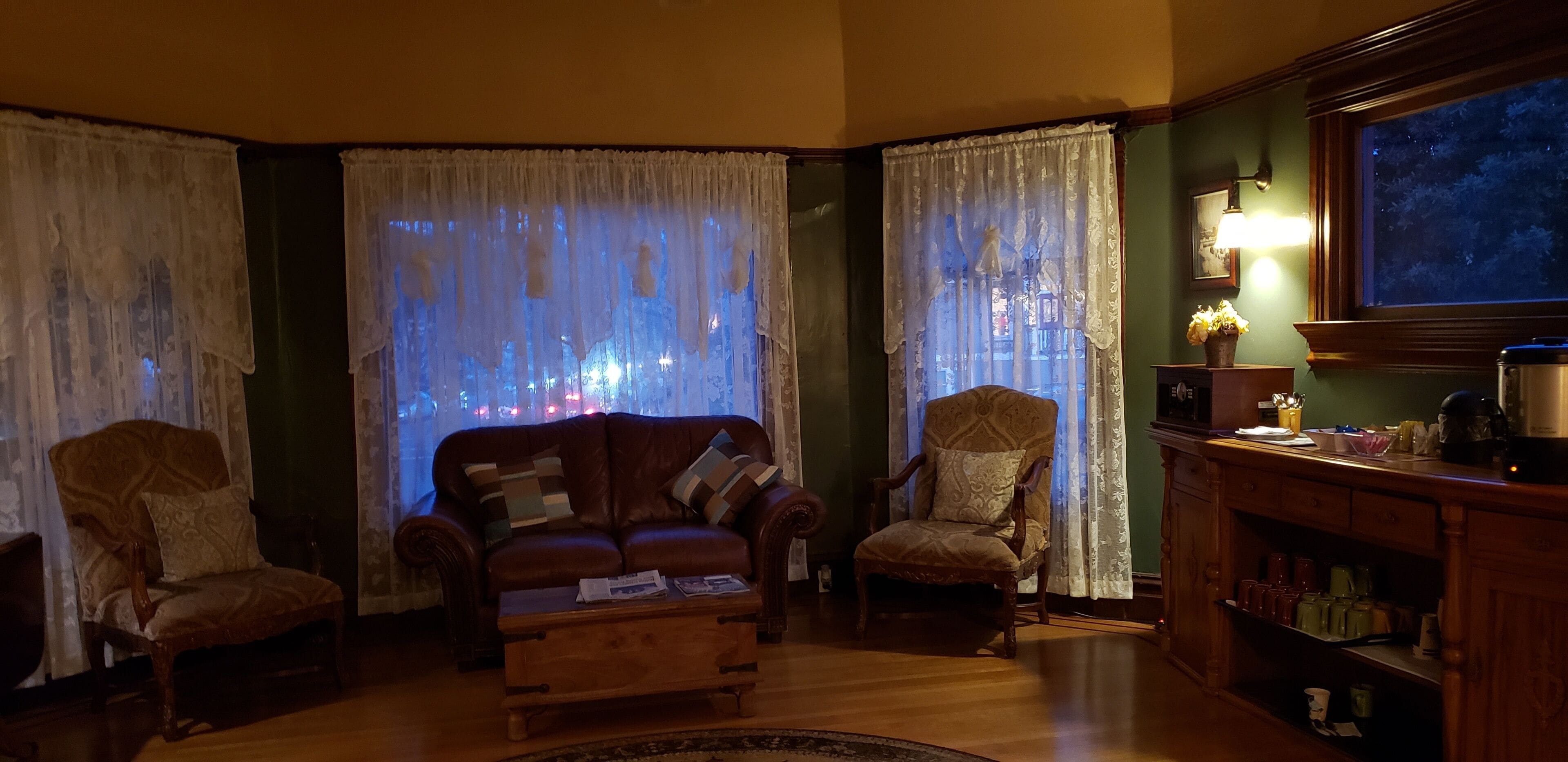 A cozy living room with a leather sofa, two armchairs, a wooden coffee table, and a sideboard with kitchenware.