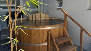 Una bañera de hidromasaje de madera con una escalera de madera que lleva a ella, rodeada de grava y plantas de bambú.