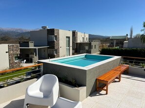 A rooftop pool with a wooden bench, a white chair, and a stone wall. - Tierras del Norte (Calderilla)