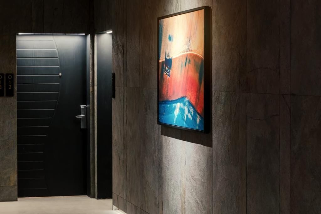 Un pasillo con una puerta negra y un cuadro abstracto enmarcado en la pared.