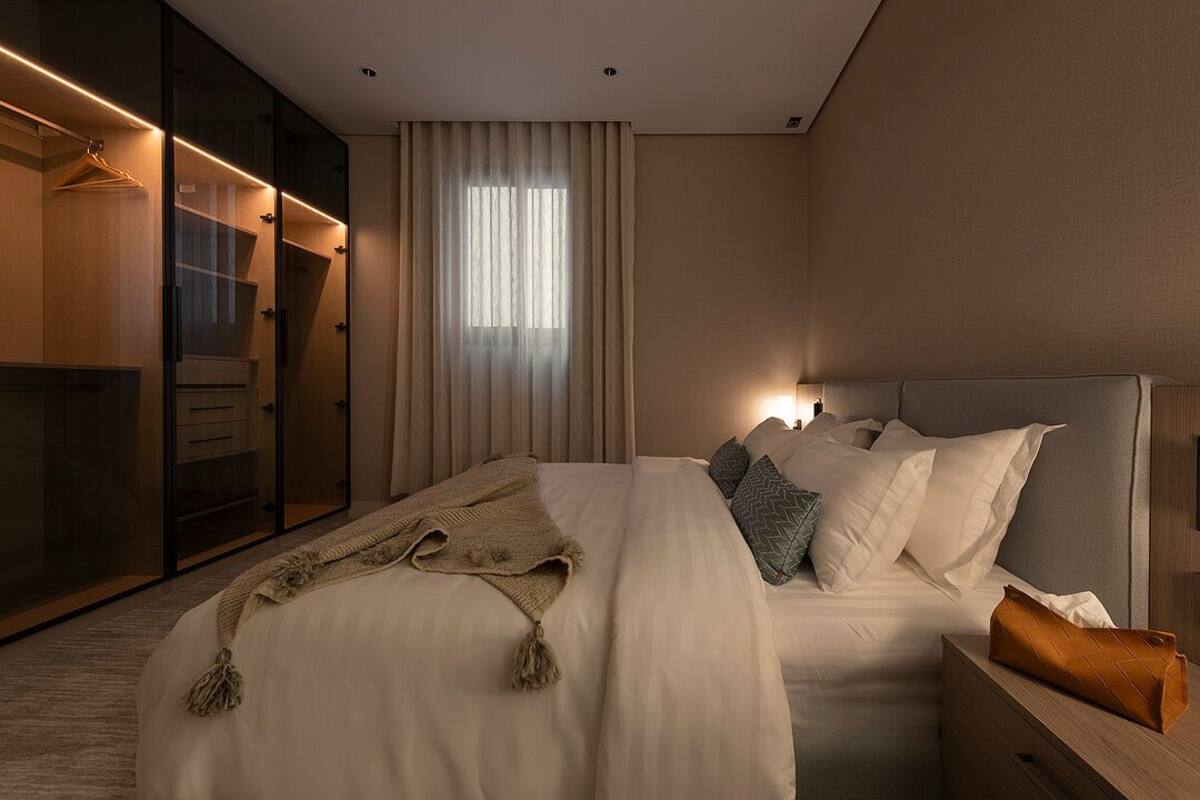 A modern bedroom with a large bed, a walk-in closet, and a window with curtains.