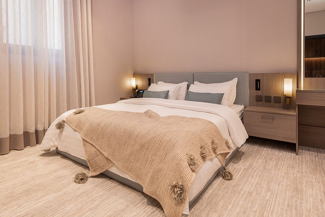 A modern hotel room with a large bed, a nightstand, a dresser, and a mirror.