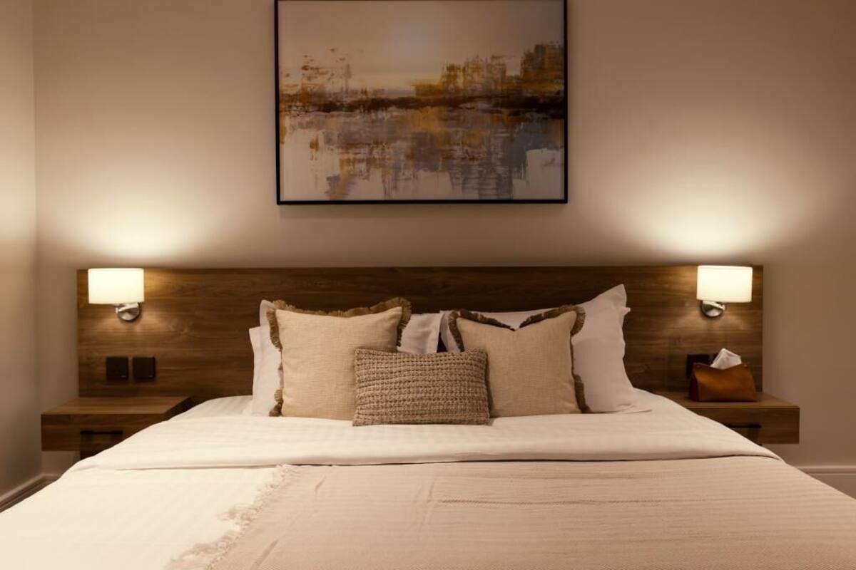 A neatly made bed with a wooden headboard, two bedside lamps, and a framed artwork above.