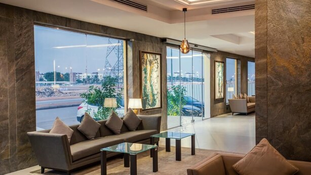 A modern hotel lobby with a sofa, coffee table, and large windows offering a view of the cityscape. - Viola Gardens Residence ( economic serviced apartments) (Riyadh)