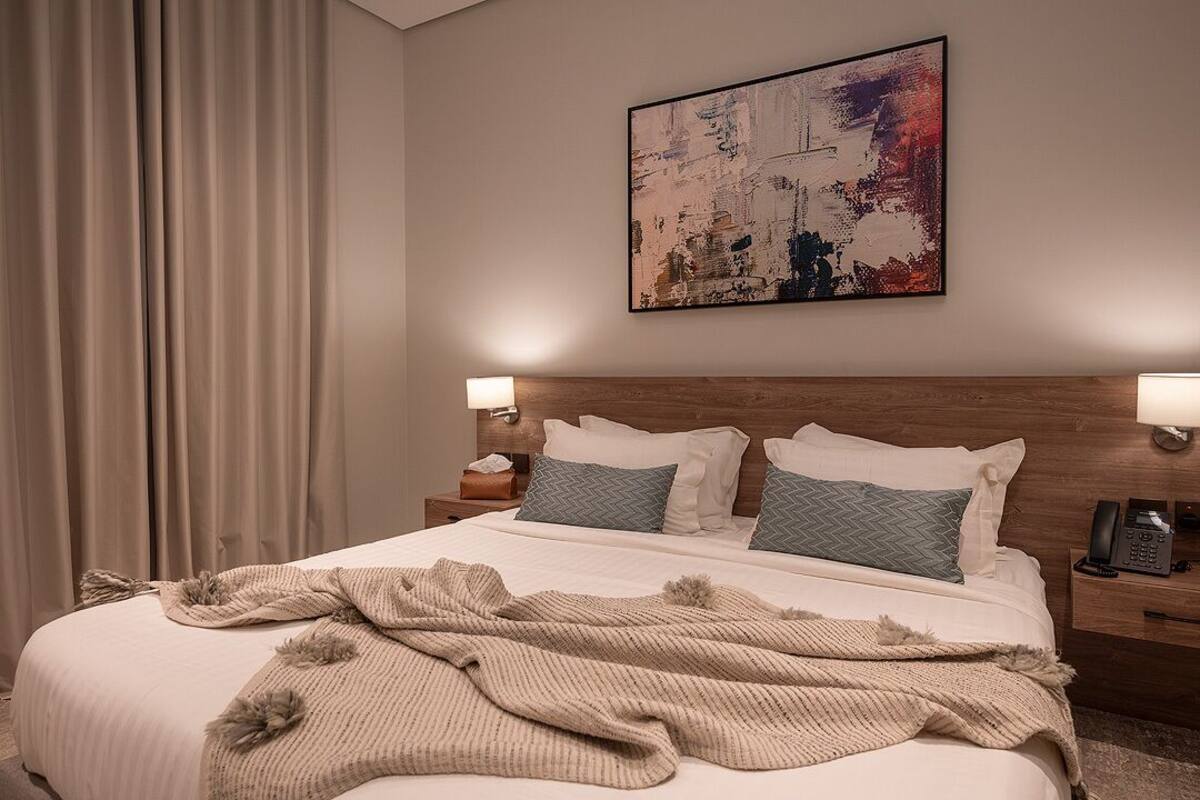 A hotel room with a large bed, two bedside tables, a wall-mounted telephone, and a painting above the bed.