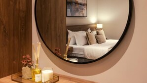 A bedroom with a round mirror, a bed with white bedding, a nightstand with candles, and a framed picture on the wall. - Viola Gardens Residence ( economic serviced apartments) (Riyadh)