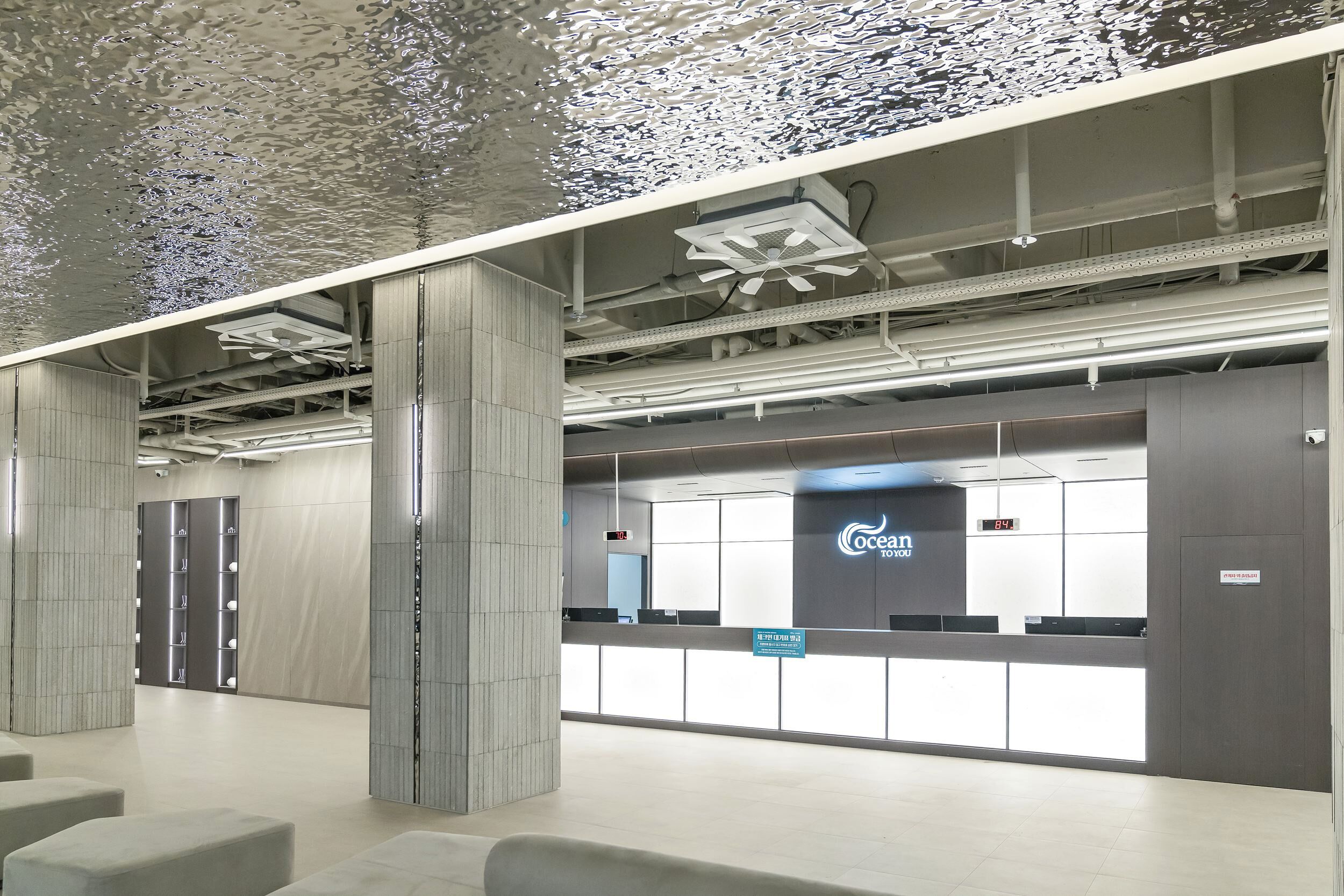 A modern, spacious lobby with a reception desk, seating areas, and a ceiling with a unique water feature.